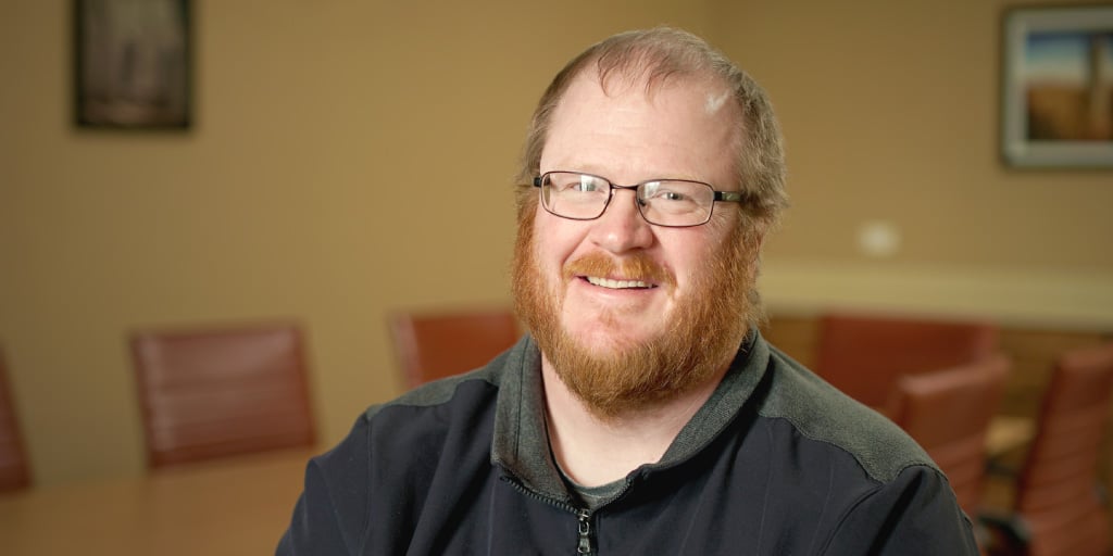 portrait of Nolen Peterson, a bearded white man wearing glasses and a black polo shirt, smiling at the camera