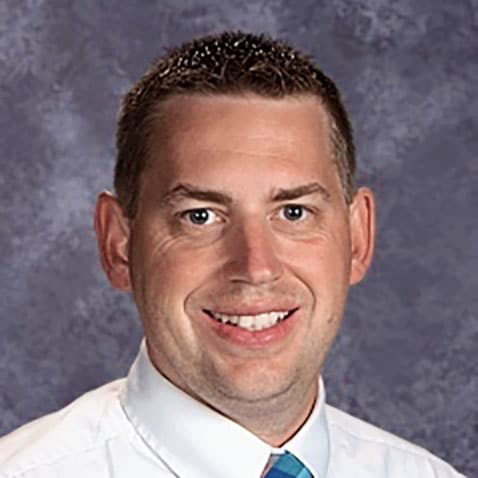 image of Travis Lape, a man with short brown hair, wearing a white collared shirt and blue tie