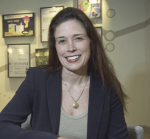 Renee Foster, a smiling woman with long brown hair in a navy blazer and gray shirt and necklace