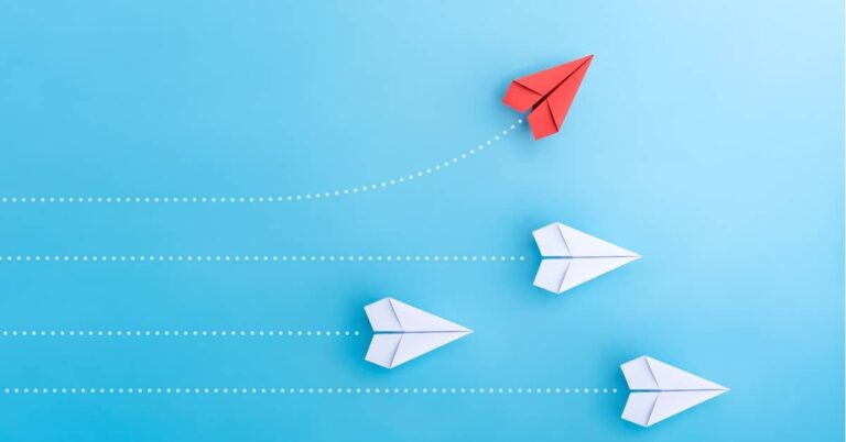four paper airplanes fly across the photo from left to right, and the top one, red, veers to the top, while the other three, white, keep going straight ahead