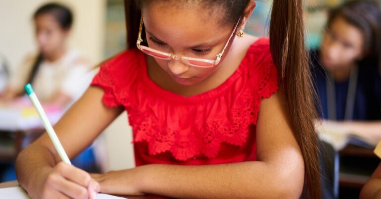 Middle-school aged girl with pigtails, red dress and glasses solving math problems at a desk