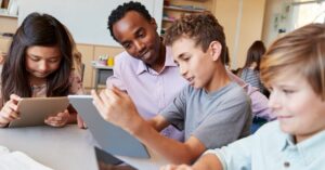 A student shows a teacher something on their mobile tablet.