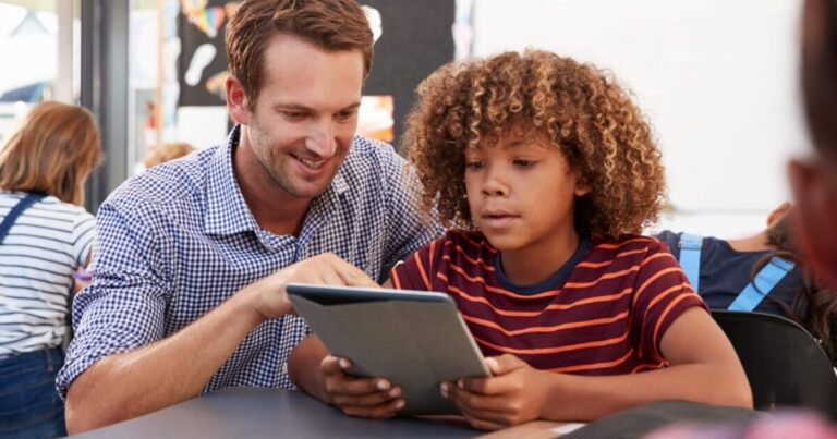 smiling teacher helps a student on a digital tablet