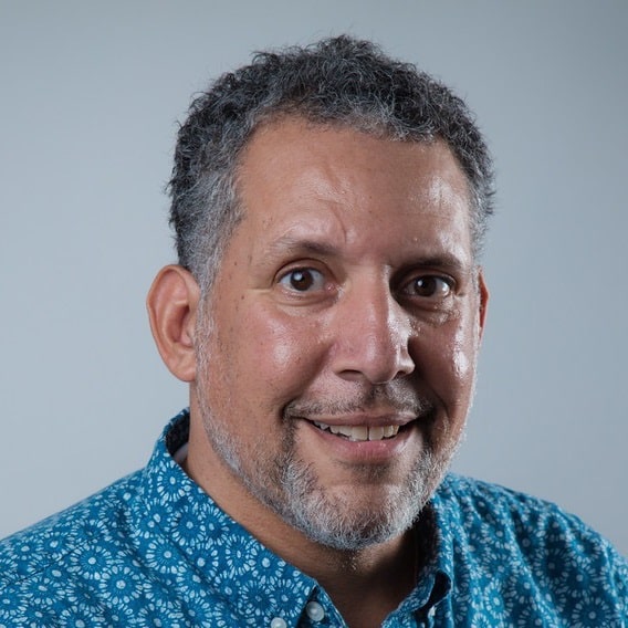 Lonny Avi Brooks, a Black, Indigenous man with short, curly gray hair, wearing a patterned blue button-up shirt