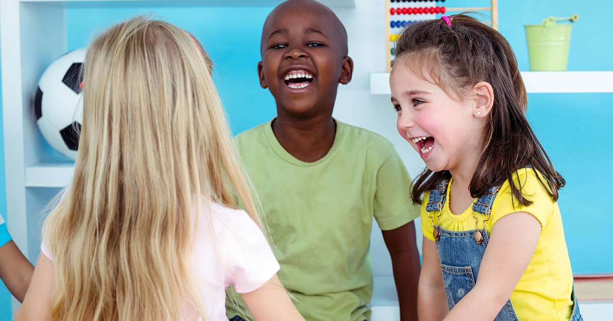 Elementary aged children, holding hands, laughing together in a bright blue room