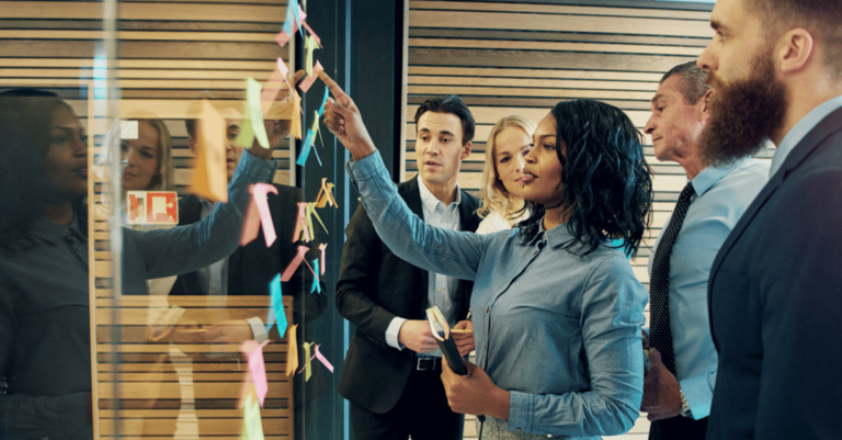 Peopel are putting up sticky notes on a glass wall for brainstorming.