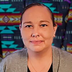 Portrait of Memorie white Mountain, an Indigenous woman with dark hair pulled back, with an Indigenous-patterned background of turquois, navy, orange and red