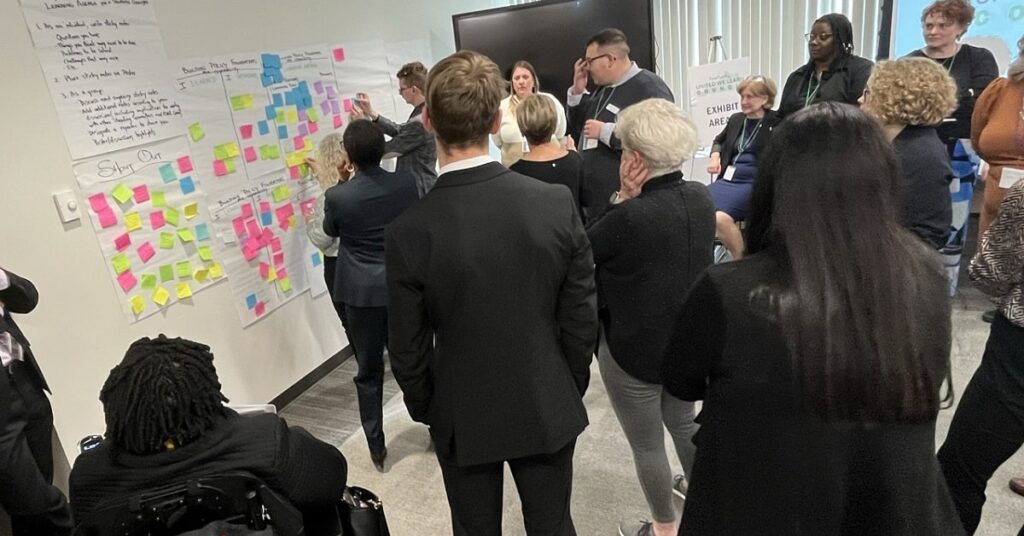 a group of diverse people convened adding sticky notes to a wall