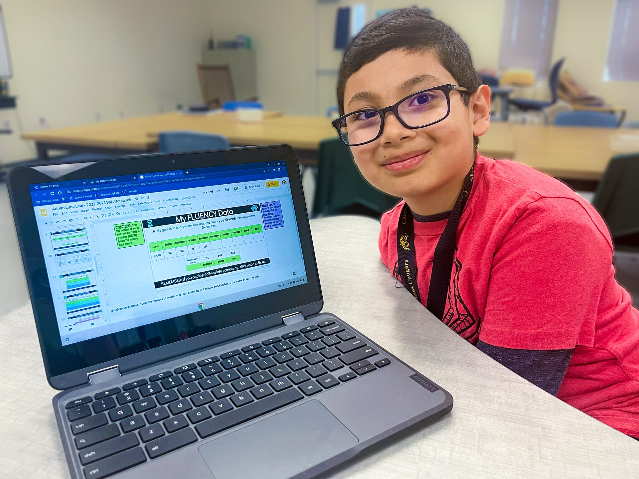 child smiling at the camera, next to a laptop