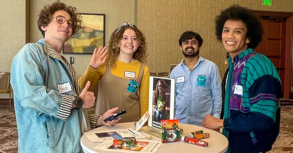 Young adults standing around a table, smiling and waving at the camera