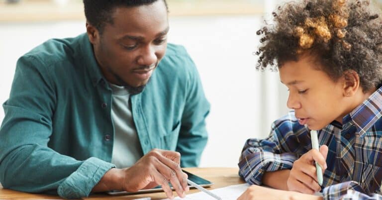 a Black man and a Black child sit at a table looking at papers together