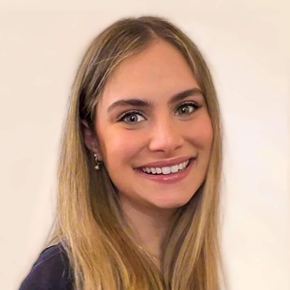 Sydni Burg, a young woman with long, straight blonde hair, smiles at the camera