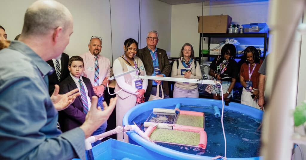 An educator shows visitors a water-based scientific lab equipment.