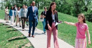 A young girl leads a tour of visiting adults on their school campus