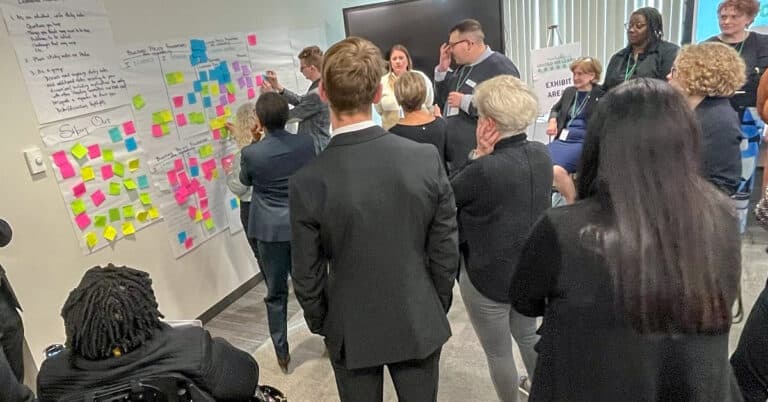 People gather at a wall of sticky notes and handwritten posters.