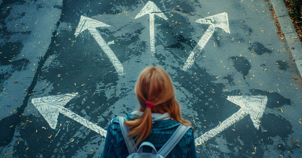 Image of a girl with red hair standing in a puddle on the road with a backpack over her shoulders, looking at arrows painted in different directions on the road