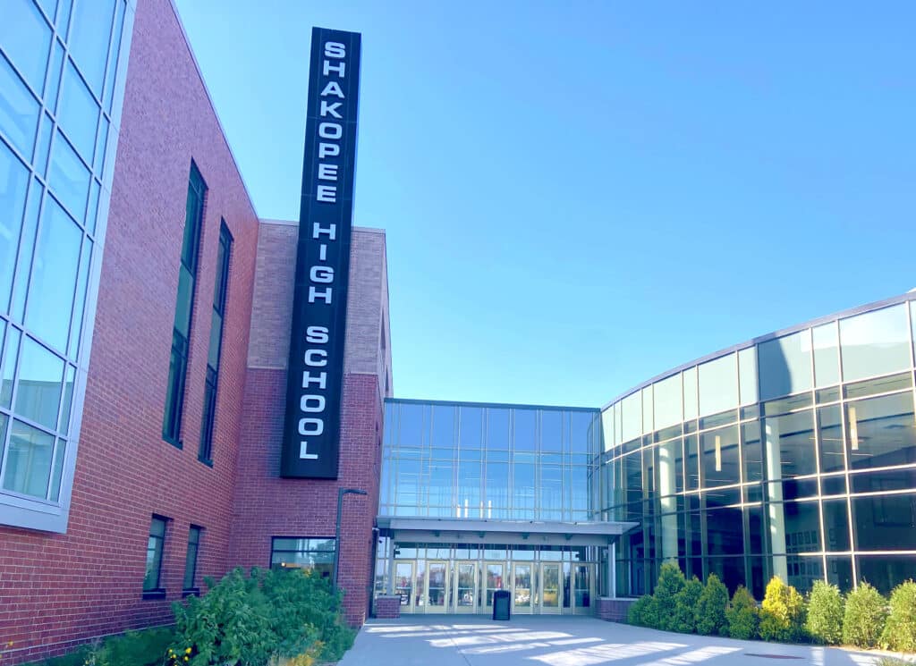 A large school building with walls of glass windows and a sign that reads, "Shakopee High School"