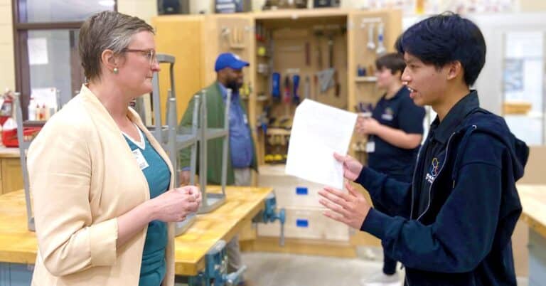 a adult woman and teen talk in a classroom with workbenches and tools