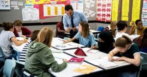 Group of students around tables learning with their teacher guiding them independently