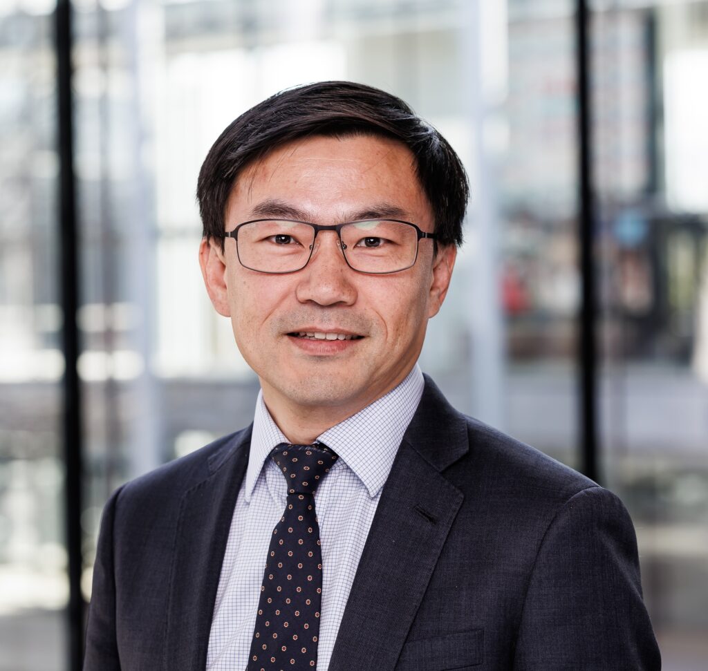Headshot of Dr. Alan Cheng, a man of Asian descent with dark hair parted at the side, wearing glasses and a navy blazer and tie and patterned button-up.