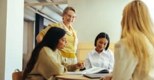 People engaging in conversation at a table with paper and a laptop in front of them
