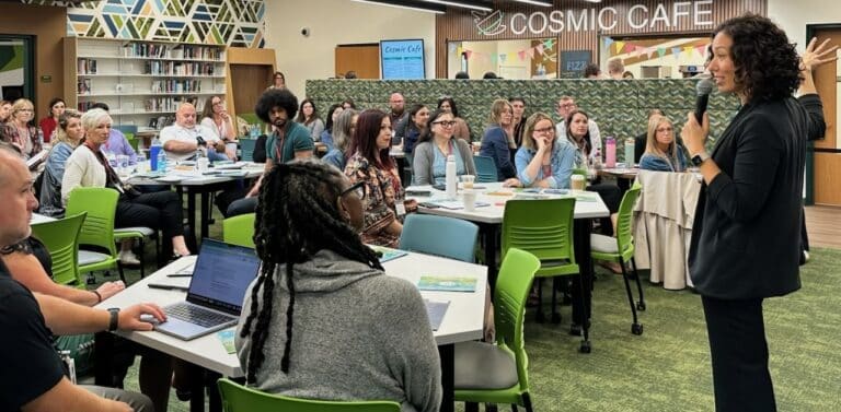 A group of educators gathers in a school library and cafe for whole-group activities