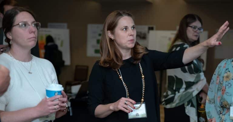 Lillian Pace extends her hand outward to talk to others about something on the wall