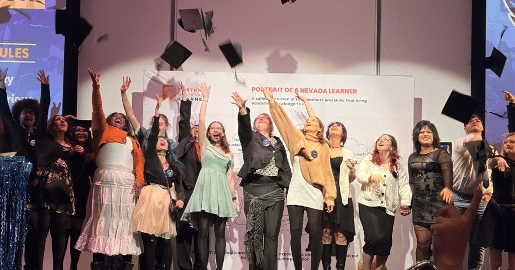Students throw graduation caps on stage, with Nevada Portrait of a Learner in the background
